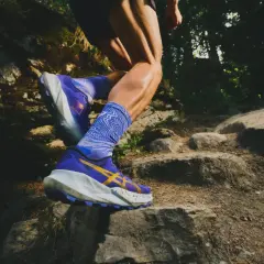Czy buty do biegania nadają się do chodzenia? Zobacz, jak sportowiec pokonuje kamienisty szlak w fioletowych butach z żółtym logo.