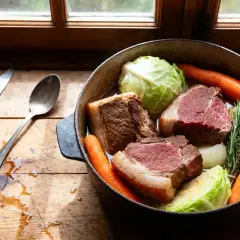 Une cocotte de potee au chou avec des morceaux de bœuf, des carottes, des oignons et des herbes, prête à mijoter.