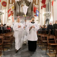 Liturgia Wielkiego Czwartku w kościele. Dwóch ministrantów w białych szatach niesie kadzidło i chorągiew.