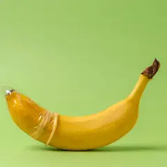 Banan w prezerwatywie, symbolizujący penis 23 cm, na zielonym tle.