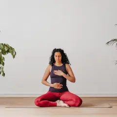 Frau sitzt im Schneidersitz auf einer Yogamatte, Hände auf Brust und Bauch. Perfekt, um mit Yoga anzufangen und innere Ruhe zu finden.