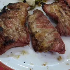 Tres trozos de secreto ibérico al horno, jugosos y con sal gruesa, servidos en un plato blanco con borde rojo.