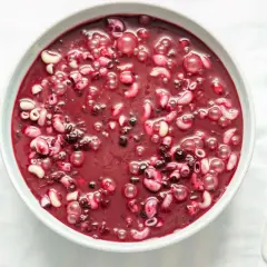 Gęsta, purpurowa zupa jagodowa z makaronem, podana w białej misce obok drewnianej łyżki.