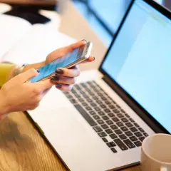 Kobieta pisze kod Swift na telefonie, obok leży laptop.