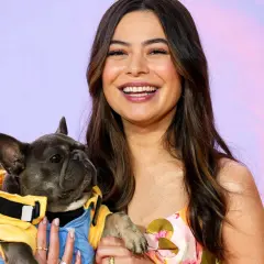 Miranda Cosgrove lächelt und hält einen französischen Bulldoggen-Welpen in einem gelben Outfit. Vielleicht ein neuer Co-Star für ihre Filme?
