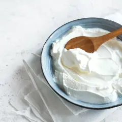 Un cuenco azul con cremoso yogur griego casero y una cuchara de madera.