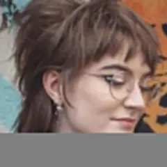 Dziewczyna w okularach z charakterystyczną, warstwową fryzurą mullet, pozuje na tle kolorowego graffiti.