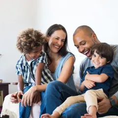 Famille souriante sur un canapé, profitant d'un moment de joie. Ce bonheur est rendu possible grâce à un **prêt conventionné** qui leur a permis d'acquérir leur foyer.
