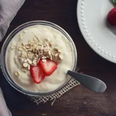 Jogurt z płatkami owsianymi i truskawkami – idealne jedzenie po wyrwaniu zęba. Na talerzyku obok leżą świeże truskawki.