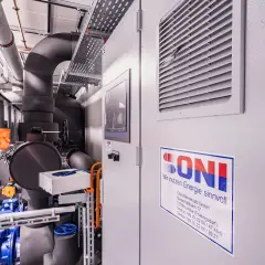 Interior de una instalación con tuberías aisladas, un gran tanque y una bomba de calor industrial.