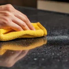 Dłoń czyści żółtą ściereczką czarny granitowy blat. Czy granit można czyścić płynem do szyb?