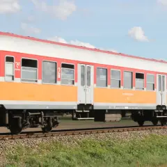 Lekki wagon pasażerski w kolorach pomarańczowo-białym i czerwonym jedzie po torach.