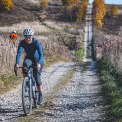Kobieta na rowerze pokonuje kamienistą drogę w jesiennych Dolinkach Krakowskich. W tle inny rowerzysta.