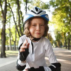 Dziecko w kasku rowerowym na głowie, gotowe do jazdy po alei w parku.