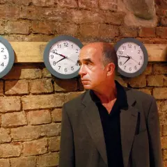 Jarosław Kozłowski wpatruje się w rząd zegarów wiszących na ceglanej ścianie.