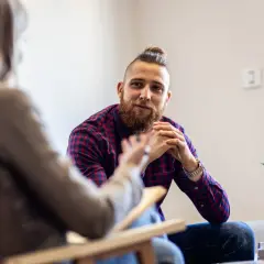 Mężczyzna z brodą i kokiem na głowie rozmawia z terapeutką, omawiając objawy ADHD u dorosłych.