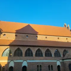 Zamek w Olsztynie, ceglana budowla z pomarańczowym dachem, pod błękitnym niebem. Wspaniałe łuki okienne i cień rzucany przez słońce.