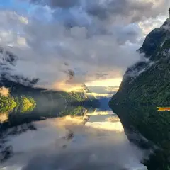 Majestatyczne fiordy norweskie, gdzie słońce przebija się przez chmury, a kajakarz przemierza spokojne wody.