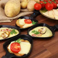 Petites poêles de raclette prêtes à être dégustées, avec pommes de terre, fromage fondu, tomates et champignons. Idéal pour savoir comment couper la raclette.