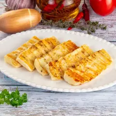 Grillowany ser halloumi na talerzu, idealny do prostych przepisów. W tle czosnek, chili i pomidory.