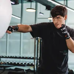 A young man practices Russian boxing, throwing a punch at a large white training bag in a modern gym.