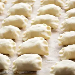 Rządki surowych pierogów z farszem na pierogi ruskie, gotowe do gotowania.