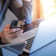 Mężczyzna z telefonem w dłoni i laptopem przed sobą. Może to być tui rezygnacja z wycieczki, bo praca wzywa.