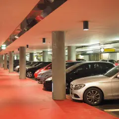 Intérieur d'un parking souterrain avec des voitures garées, sol rouge vif, éclairage artificiel. Un parking pratique pour explorer Venise.