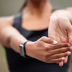 Kobieta rozciąga nadgarstki, ćwicząc jak wzmocnić nadgarstki. Zegarek sportowy na ręce.