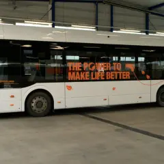 Ein weißer, moderner elektrischer Bus steht in einer Halle. Auf der Seite steht "THE POWER TO MAKE LIFE BETTER" und "100% ELECT".