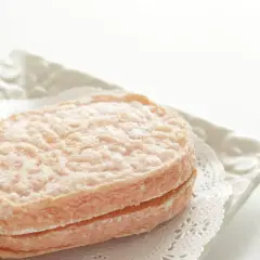 Delicato dacquoise alle nocciole, un dolce leggero e friabile, servito su un piatto bianco con un centrino di pizzo.