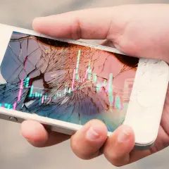 Dłoń trzyma pęknięty smartfon z wykresem giełdowym. Ubezpieczenie ekranu to spokój ducha.