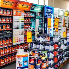W sklepie z farbami Dulux, półki uginają się pod ciężarem kolorowych puszek. Widać próbnik kolorów i promocje na farby.