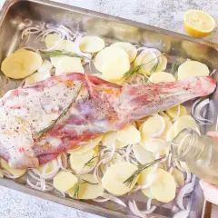 Paletilla de cordero al horno lista para asar con patatas, cebolla y romero. Un chorrito de aceite y al horno.