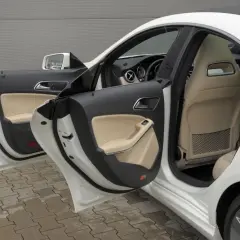 Biały Mercedes CLA 180 z otwartymi drzwiami, widoczne jasne wnętrze i czarne panele drzwi.