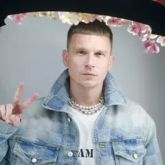 Bart Pniewski, młody mężczyzna w jeansowej kurtce, pozuje z uniesionym znakiem pokoju.