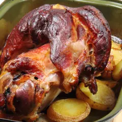 Pieczona golonka z ziemniakami w zielonej brytfannie.