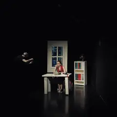 Scena w **teatrze Kana Szczecin**: kobieta przy biurku rozmawia przez telefon, mężczyzna w tle filmuje.