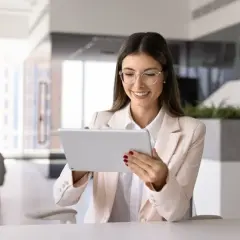 Uśmiechnięta kobieta w okularach przegląda tablet, zastanawiając się, czy umowa zlecenie wlicza się do stażu pracy.