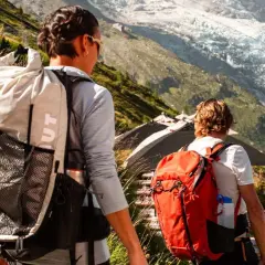 Zwei Wanderer mit Rucksäcken auf einem Bergpfad. Die Frage "was zieht man zum wandern an" wird durch ihre funktionale Kleidung beantwortet.
