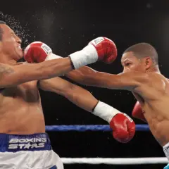 Two boxers in the minimum weight category exchange blows in a tense match. One fighter recoils as a punch lands, sending sweat flying.