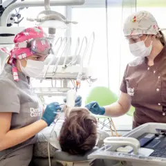 Dwie dentystki w maskach i okularach pracują przy pacjencie. Jedna z nich trzyma narzędzie, druga monitoruje. Szybkie bicie serca po znieczuleniu u dentysty to częsty objaw.
