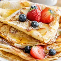 Ein Stapel goldbrauner Pfannkuchen, bestäubt mit Puderzucker und garniert mit frischen Beeren und Honig. Ein einfaches Pfannkuchen-Rezept, das jeden Tag zum Genuss macht.