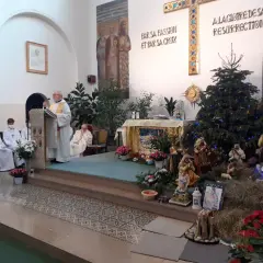 Uroczystość w kościele z kapłanem przy pulpicie i szopką bożonarodzeniową. Święta Genowefa w centrum uwagi.
