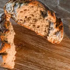Ein aufgeschnittenes Brot, ein starkes Symbol für Nahrung und Leben, liegt neben einem Glas Wasser auf einem Holztisch.