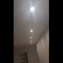 W korytarzu domu widać rząd wbudowanych w sufit lamp. Jedna z nich, najbliżej widza, świeci najjaśniej, tworząc efekt migającego światła.