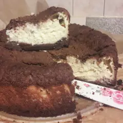 Pyszny sernik królewski bezglutenowy z czekoladową kruszonką i kremowym nadzieniem. Pokrojony kawałek czeka na spróbowanie.