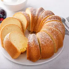 Pyszna babka piaskowa, jak z przepisu babci, posypana cukrem pudrem, z owocami i widelcami obok.