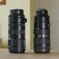 Two Nikon telephoto lenses, including a Nikkor 200mm f2, stand side-by-side on a wooden table.