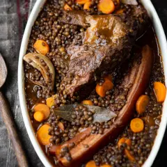 Un plat réconfortant de petit salé aux lentilles, avec des morceaux de viande savoureux, des carottes et des oignons, prêt à être servi.